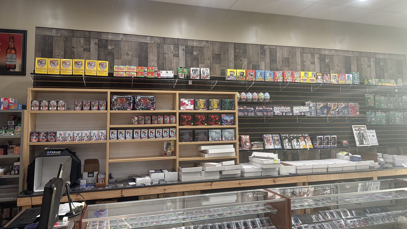 The sealed box wall in Kearney: current hobby and blaster boxes on the shelves, vintage wax racked along the top rail above them.